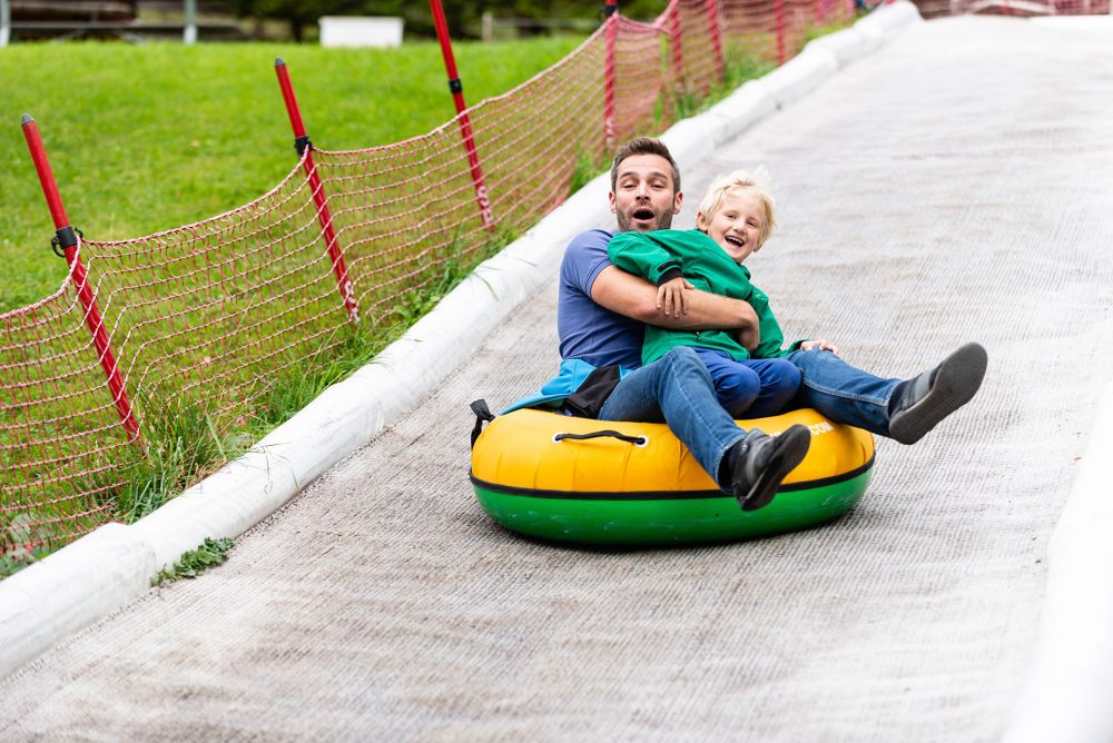 Ein Vater rutscht mit seinem Sohn im Arm auf einem Schlauchreifen bergab.