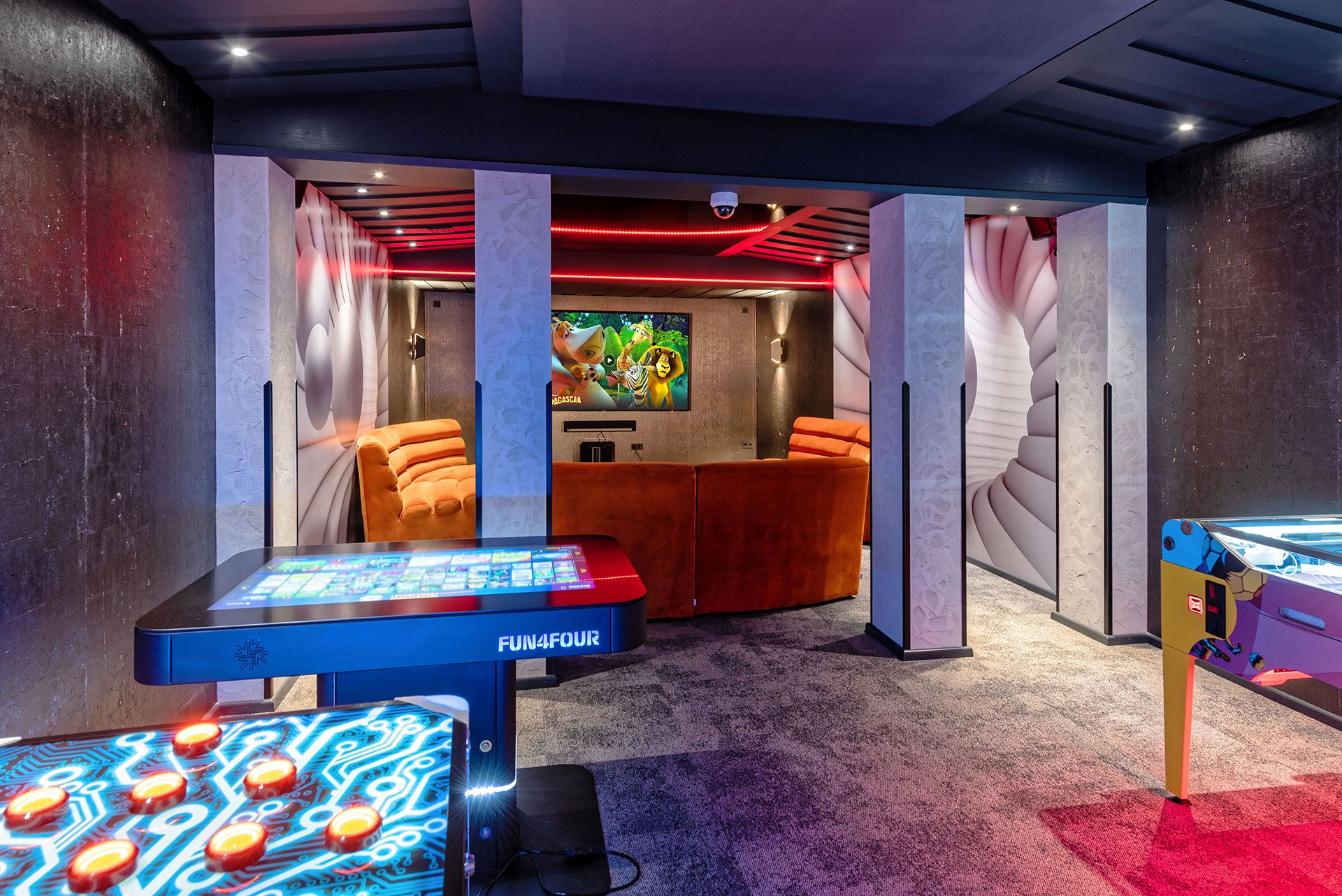 Room with a large TV on the wall and seating around it, in the foreground 3 