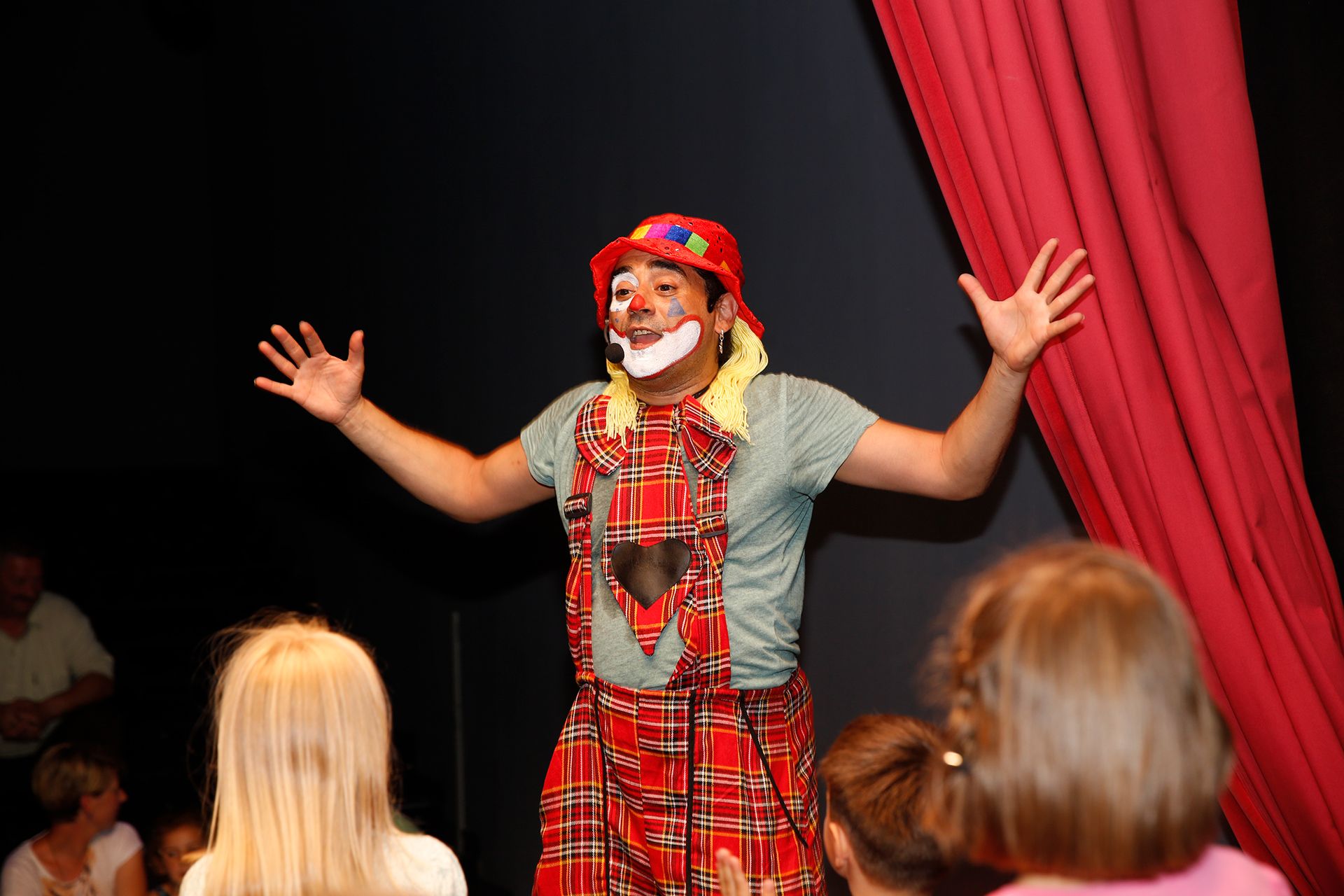 A man dressed as a clown standing on a stage and performing in front of children.