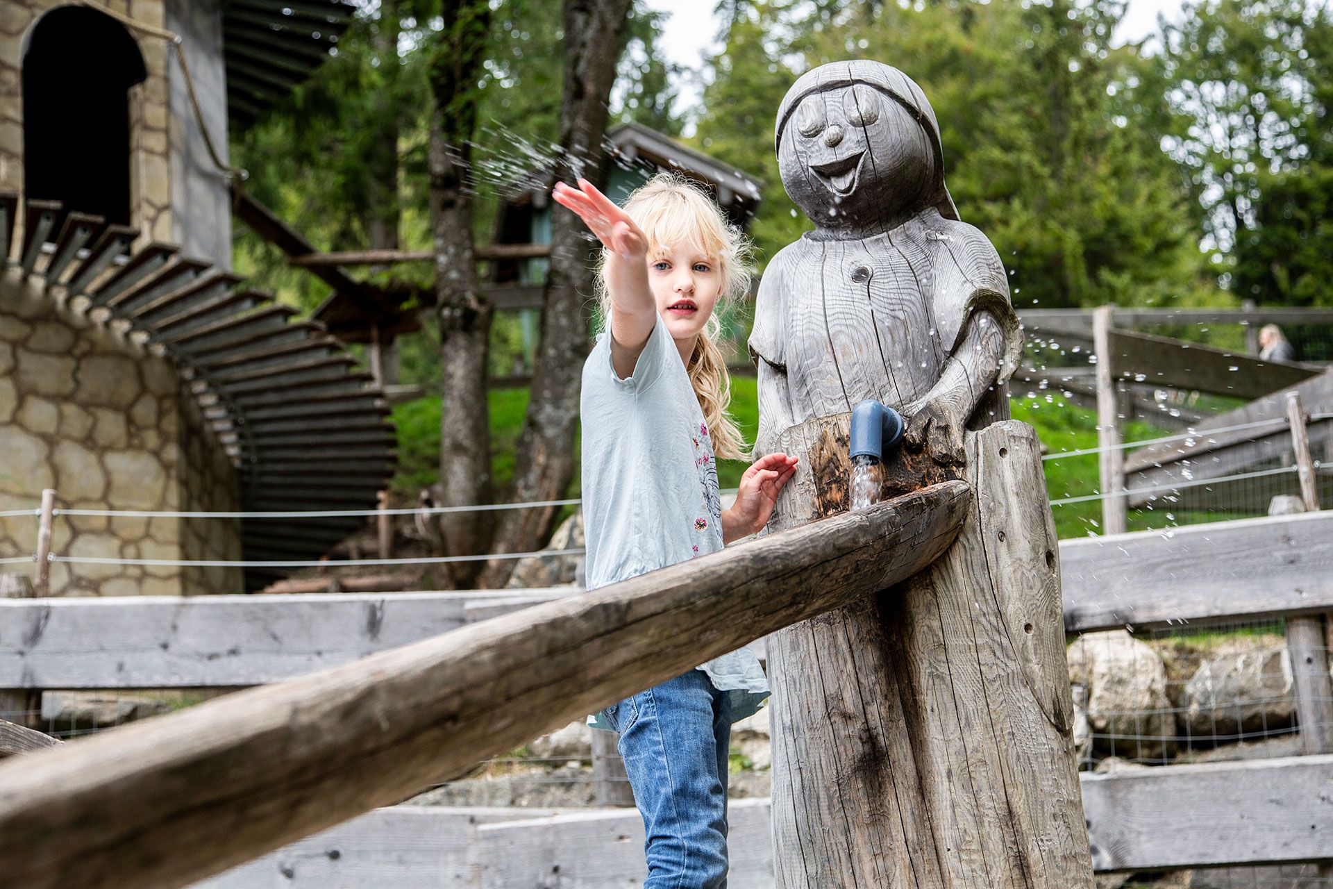 Ein junges Mädchen schnipst Wasser aus einem Brunnen in Form einer lustigen Figur umher.