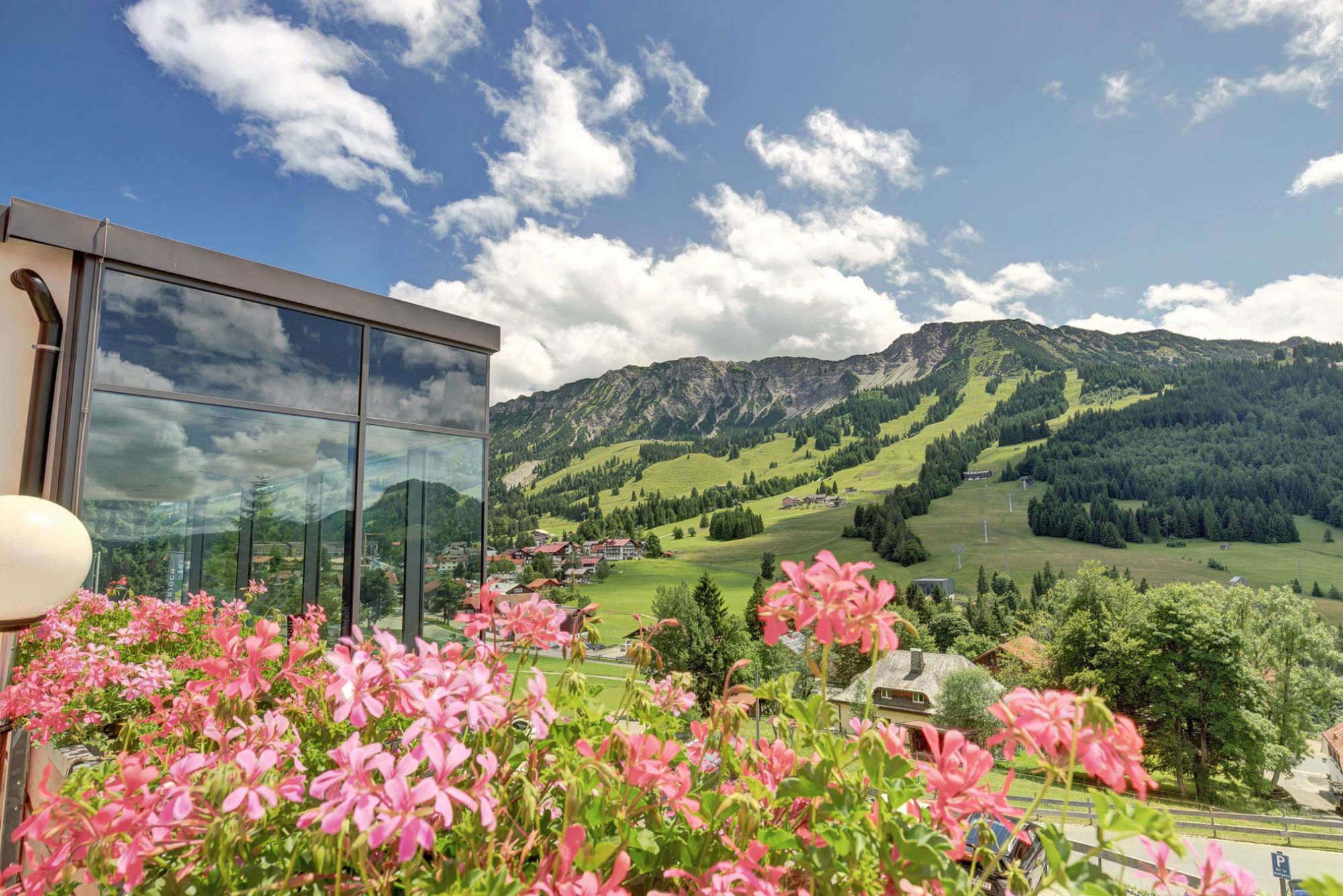 On the left in the image is the corner of the 4-star Allgäu Hotel, flowers in the foreground, mountains in the background.
