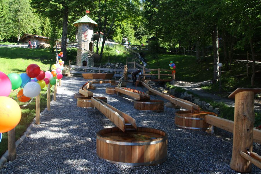 Outdoor-Wasserspielplatz mit Wasserrutschen aus Holz, links im Bild Luftballons an mehreren Pfosten. Outdoor-Wasserspielplatz mit Wasserrutschen aus Holz, links im Bild Luftballons an mehreren Pfosten.