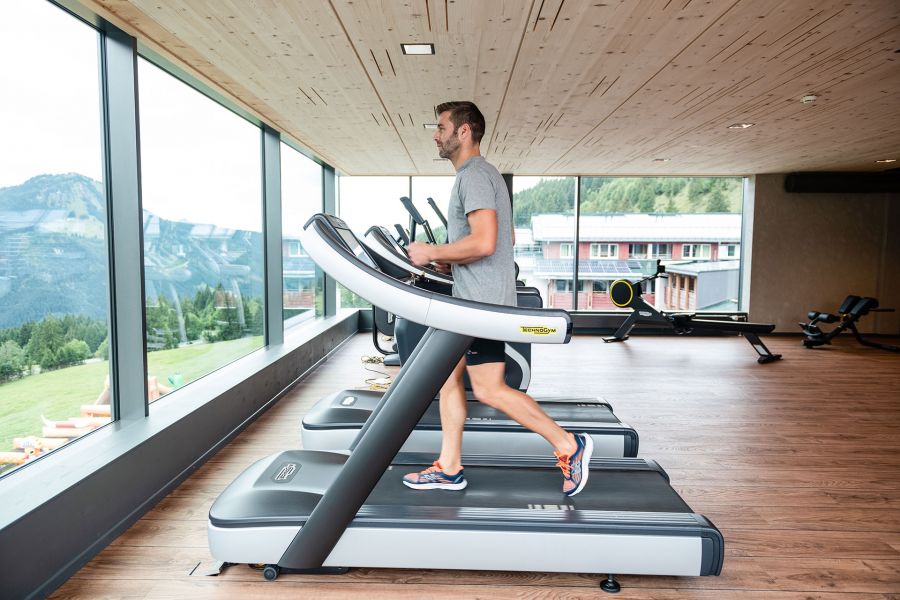 Gym with exercise equipment, a man running on a treadmill, looking through the panoramic windows at the mountains. Gym with exercise equipment, a man running on a treadmill, looking through the panoramic windows at the mountains.